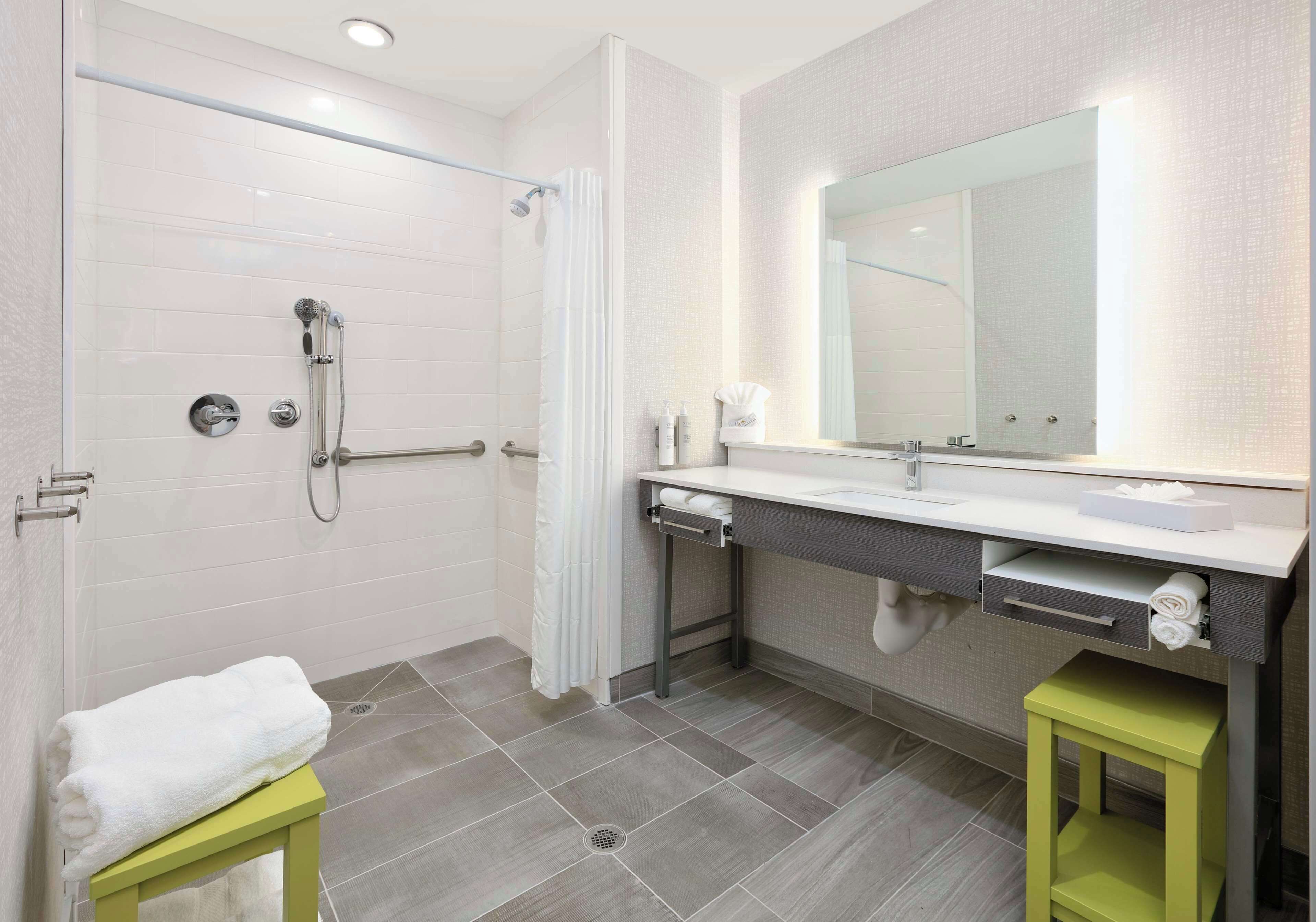 A modern bathroom with a shower, a sink with a mirror, and a green stool.