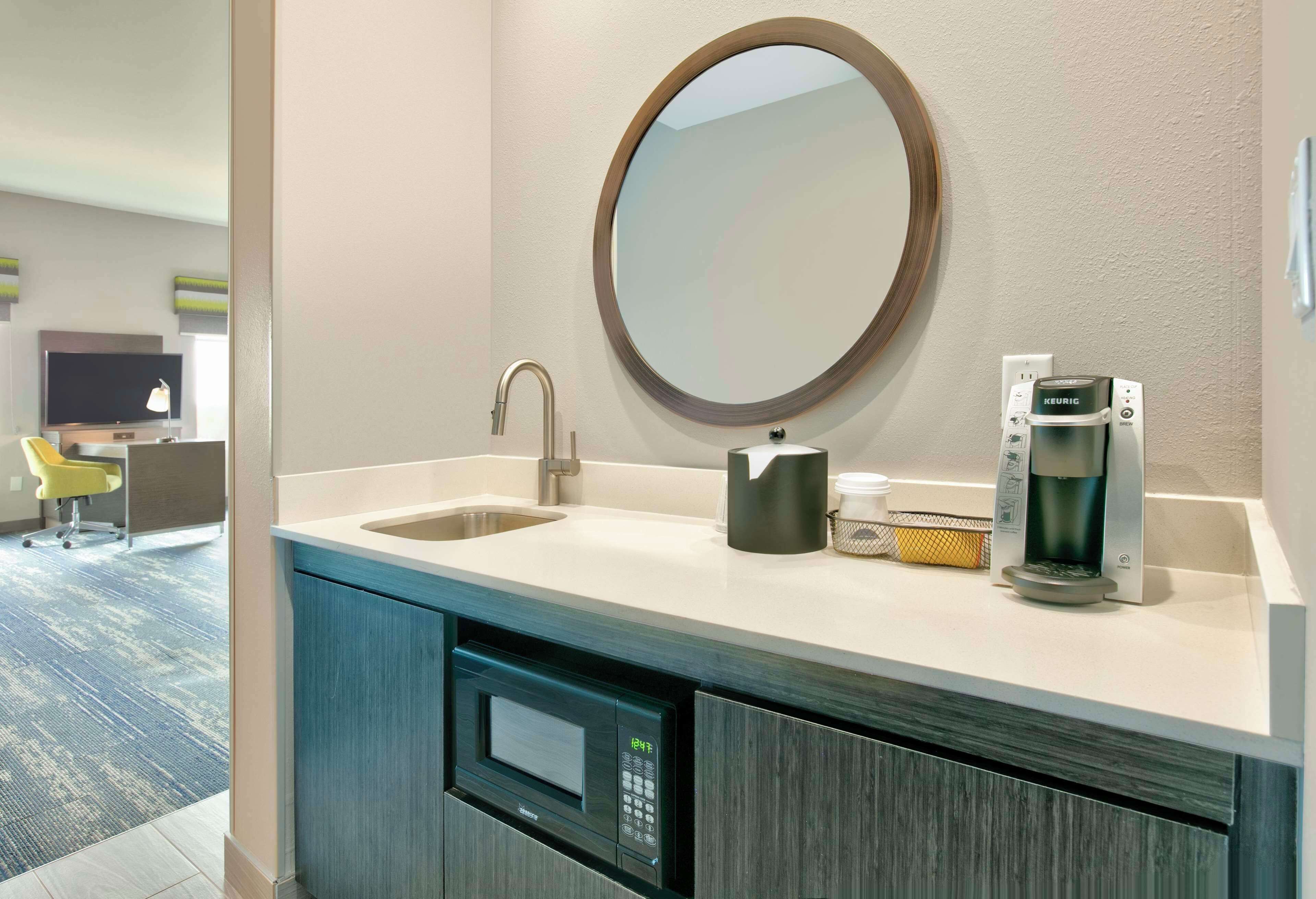 Un baño moderno con lavamanos, espejo, cafetera y microondas integrado.