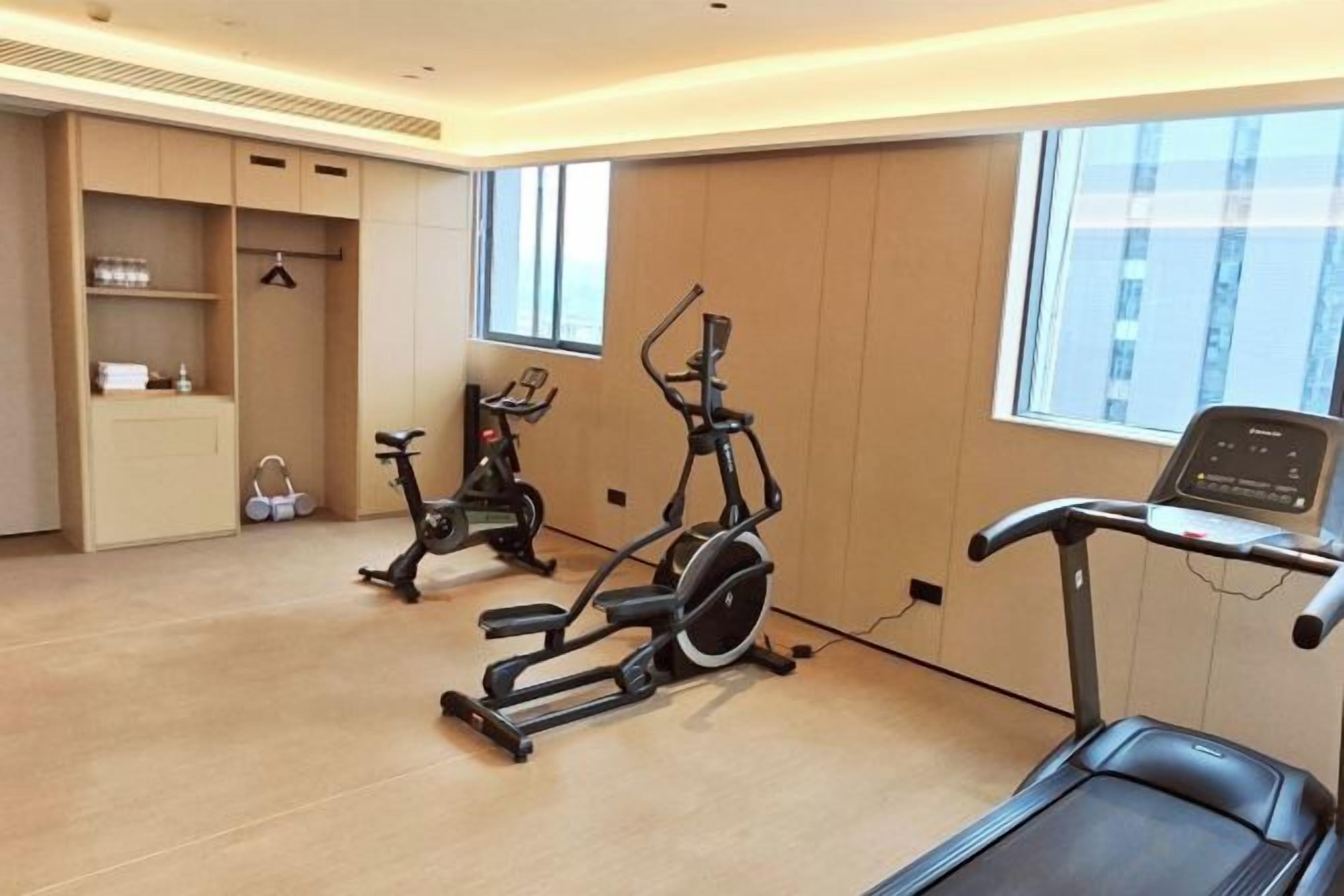 A room with exercise equipment including a treadmill and stationary bikes, a window with a view, and a built-in cabinet.