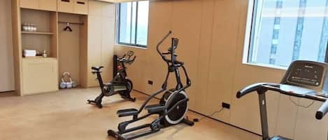 A room with exercise equipment including a treadmill and stationary bikes, a window with a view, and a built-in cabinet.