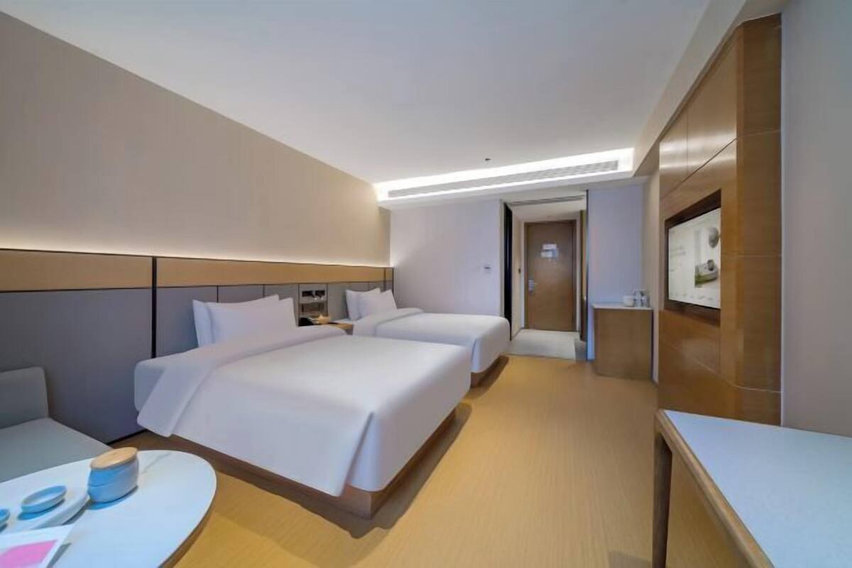 A hotel room with two beds, a desk, a chair, and a television.
