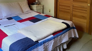 Une chambre à coucher avec un lit, une table de chevet, une lampe, un tableau encadré et une porte en bois.