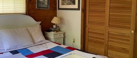 Une chambre à coucher avec un lit, une table de chevet, une lampe, un tableau encadré et une porte en bois.