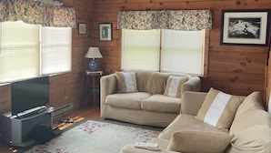 L’intérieur chaleureux d’un chalet avec des murs en bois, un canapé beige, un téléviseur et un tapis à motifs floraux.