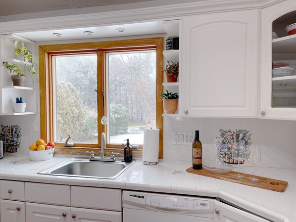 Enjoy a kitchen with a large window offering a view of the surrounding area, stainless steel sink, and white cabinetry.