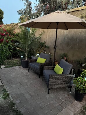 A patio with two wicker chairs, a large umbrella, and potted plants. - Private studio with  large patio (Santa Barbara)