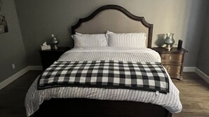 A bedroom with a large bed, a nightstand, a wall decoration, and a wooden floor. - Cozy Farmhouse Style - Pet Friendly (Bullhead City)