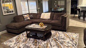 A living room with a sectional sofa, a coffee table with a vase of sunflowers, and a patterned rug. - Cozy Farmhouse Style - Pet Friendly (Bullhead City)