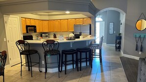 A kitchen with a central island, wooden cabinets, and a bar area with stools. - Cozy Farmhouse Style - Pet Friendly (Bullhead City)