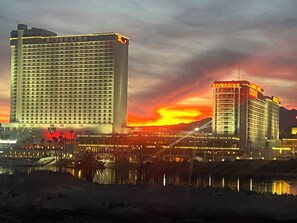 Un grand hôtel avec une enseigne bien visible au bord de la rivière, de nombreux étages et une vue sur le coucher de soleil au-dessus d’une étendue d’eau.