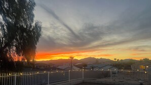 A fenced outdoor area with a fire pit, surrounded by residential buildings and a sunset view. - Cozy Farmhouse Style - Pet Friendly (Bullhead City)