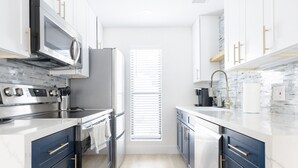 A modern kitchen with stainless steel appliances, white cabinets, and a window with blinds. - Quiet 2BR - 10 Min Walk to Old Town (Scottsdale)