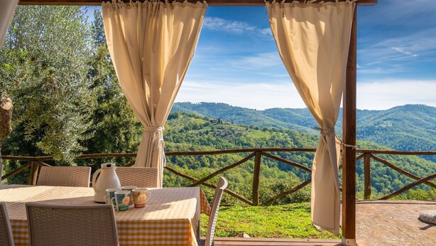 Un espace extérieur aménagé avec une table et des chaises, offrant une vue sur des collines verdoyantes, et agrémenté d’une structure en forme de pergola en bois.