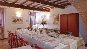 Un espace repas avec une longue table dressée pour accueillir plusieurs convives, des poutres en bois au plafond et un mur en briques.