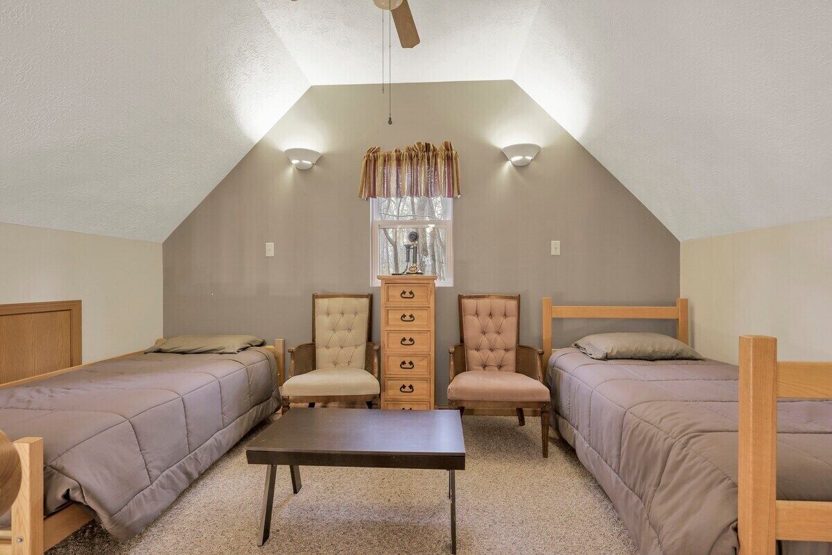 Habitación tipo dormitorio con dos camas individuales, un aparador de madera, una mesa y un ventilador de techo.