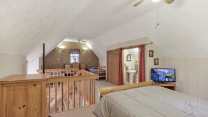 A bedroom with a sloped ceiling, a wooden bed, a television, and a small desk with a chair. - Gray Manor (Hocking Hills Area) (Rockbridge)