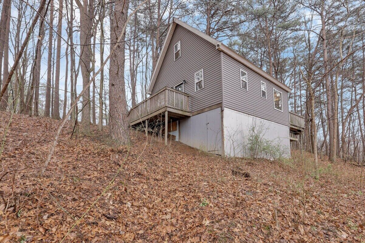 A two-story house with a balcony, surrounded by trees and a wooded area.