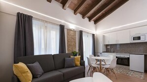 Ein modernes Wohnzimmer mit einer Couch, einem Esstisch und Stühlen. Es gibt eine Küchenzeile mit weißen Schränken und einer Mikrowelle.