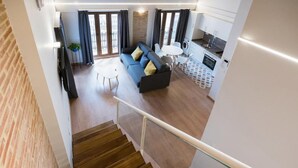 Eine moderne Wohnung mit einer Treppe, die in einen Wohnbereich mit Sofa, Esstisch und Küchenzeile mit Kühlschrank und Waschmaschine führt.