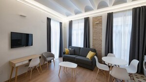 Een moderne woonkamer met een bank, een televisie, een bureau en een eethoek.
