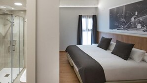 Een moderne hotelkamer met een groot bed, een douchecabine van glas en een ingelijst schilderij aan de muur.
