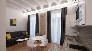 Een moderne woonkamer met een bank, een eettafel, stoelen en een keukenhoek met een spoelbak en magnetron.