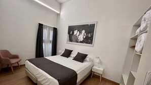 Ein modernes Schlafzimmer mit einem großen Bett, einem Nachttisch mit Lampe, einem Sessel und einem Kleiderschrank.