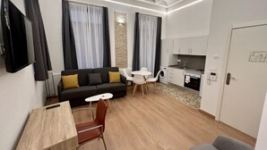 Ein kompakter Wohnbereich mit einer Couch, Esstisch, Stühlen, einem Fernseher und einer Küchenzeile.