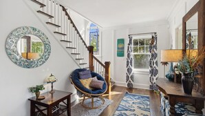 A staircase with wooden railings, a blue chair with cushions, a round mirror, and a patterned rug.