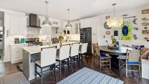 A modern kitchen with white cabinetry, a central island with bar stools, and pendant lighting.