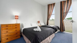 Une chambre d’hôtel avec deux lits, une commode en bois et une fenêtre avec des rideaux.