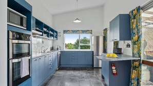 Une cuisine moderne avec des meubles bleus, une grande fenêtre et une vue sur la verdure environnante.