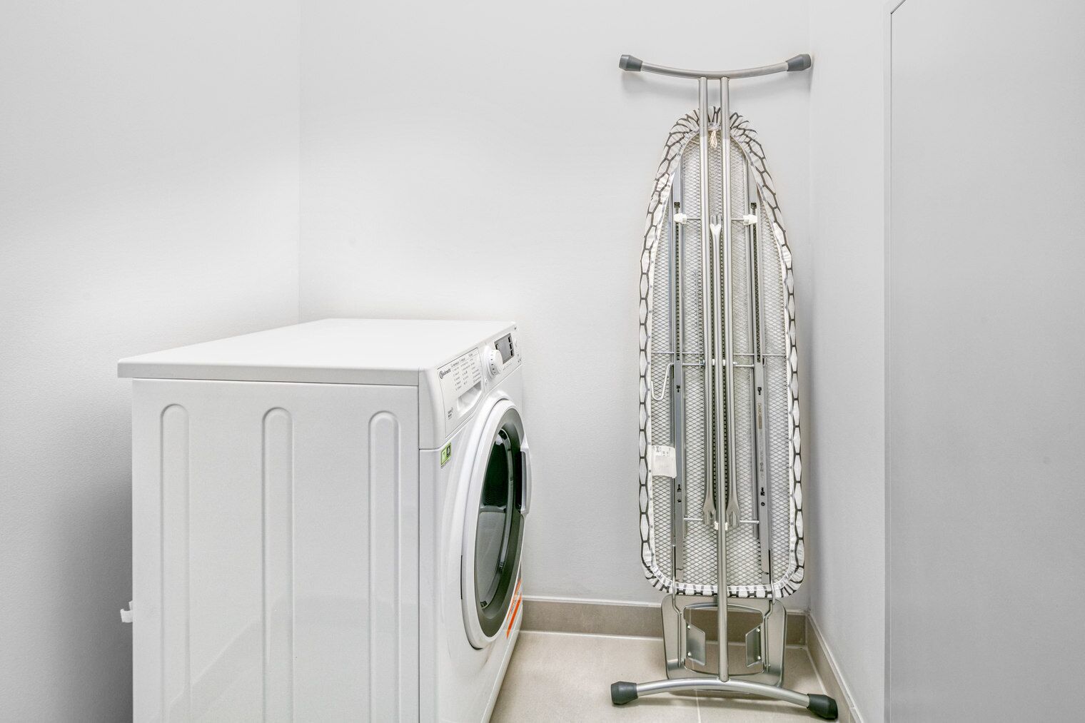 A compact laundry area with a washing machine and a wall-mounted ironing board.