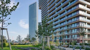 Un bâtiment moderne à étages, doté de grandes fenêtres et d’un jardin bien entretenu, agrémenté d’arbres et d’un sentier.