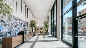 Un hall d’hôtel moderne doté d’un comptoir d’accueil, d’un espace salon et de grandes fenêtres offrant une vue sur la ville.