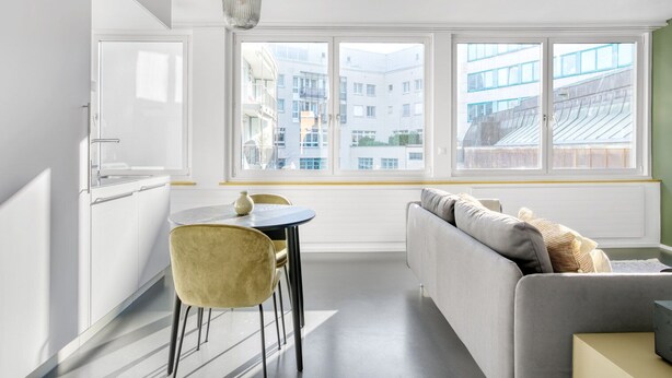 Una cucina moderna con mobili bianchi, un tavolo da pranzo con due sedie e un divano con cuscini.