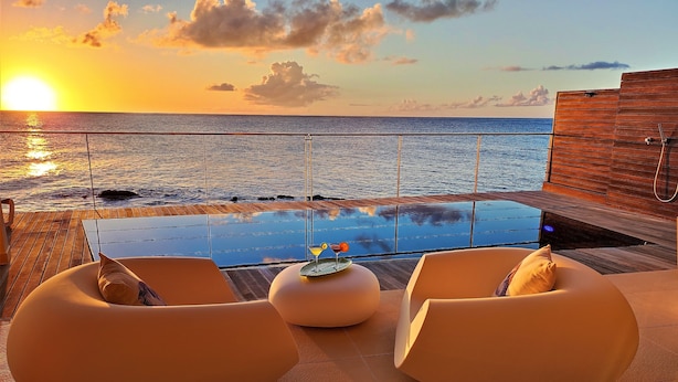 Vista al atardecer desde un balcón con piscina y dos sillones de relax.