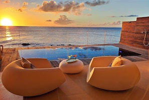 Une vue sur le coucher de soleil depuis un balcon avec une piscine et deux chaises longues.