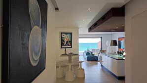Un interior moderno con un cuadro abstracto grande, un comedor con mobiliario blanco y vista al mar.