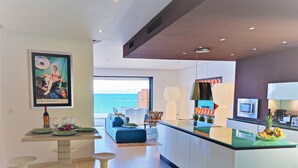 Una cocina moderna con una isla central, un comedor con mesa y sillas, y vista al mar a través de amplios ventanales.