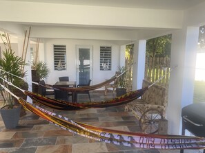 A hammock in a covered outdoor area with a table and chairs, potted plants, and a wooden cart. - Cozy tropical paradise- 1min from the beach! (Río Grande)