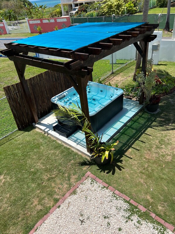 A hot tub under a wooden pergola in a backyard with a pool, surrounded by plants and a fence. - Cozy tropical paradise- 1min from the beach! (Río Grande)