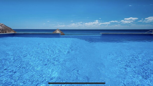 Een helderblauw zwembad met uitzicht op de oceaan en een rieten constructie op de achtergrond.