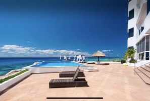 A pool area with lounge chairs, a thatched umbrella, and a view of the ocean.