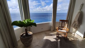 Een balkon met een bloempot, een houten stoel en uitzicht op de oceaan.