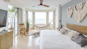 Een ruime slaapkamer met een groot bed, een hangmat, een televisie en uitzicht op de oceaan.