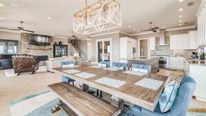 A spacious kitchen with a large island, a dining area with a wooden table and blue upholstered chairs, and a stone fireplace.