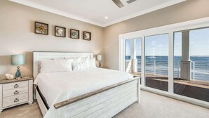 A bedroom with a large bed, a ceiling fan, and a balcony with a view of the ocean.