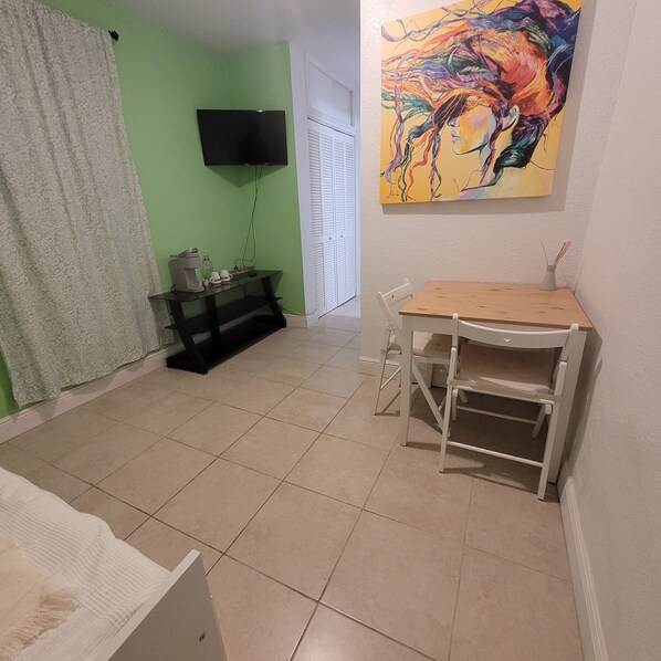 Une pièce avec un mur vert, un téléviseur à écran plat fixé au mur, une petite table avec une chaise et un tableau au-dessus de la table.