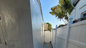 Un passage étroit et fermé, bordé d’une clôture blanche d’un côté et d’une porte de l’autre.